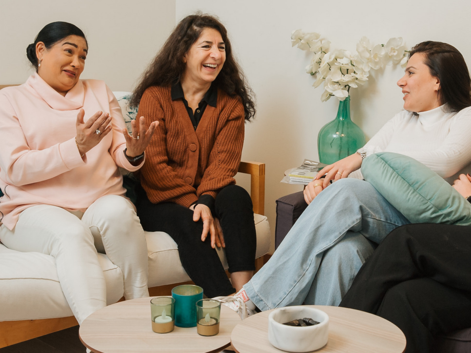 Drie vrouwen praten en lachen in de woonkamer.